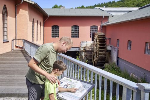 Vater und Sohn lesen ein Infoschild vor einem Museum