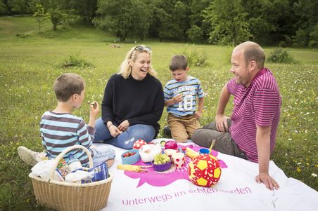 Familie sitzt im Gras und macht ein Picknick