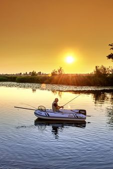 Angler sitzt im Boot bei Sonnenaufgang