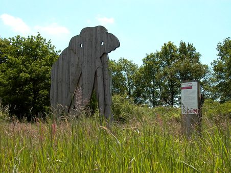 Elefantenholzstatue mit Infotafel im hohen Gras
