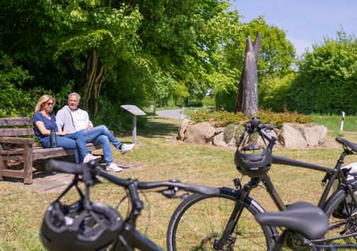 Zwei Radfahrer machen eine Pause vor einem Ochsenwegdenkmal